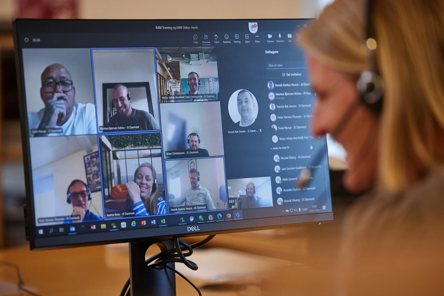A woman attending a teams meeting at JS Danmark. The woman wears a headset and smiles at her colleagues.